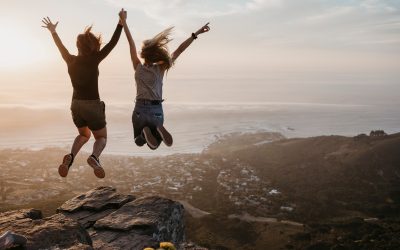 South Africa, Cape Town, Kloof Nek, two women jumping on rock at sunset
